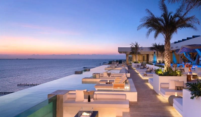 Unik the Kitchen rooftop infinity pool and oceanfront lounge area with a fire pit at twilight at Impression Isla Mujeres by Secrets by Kenwood Travel