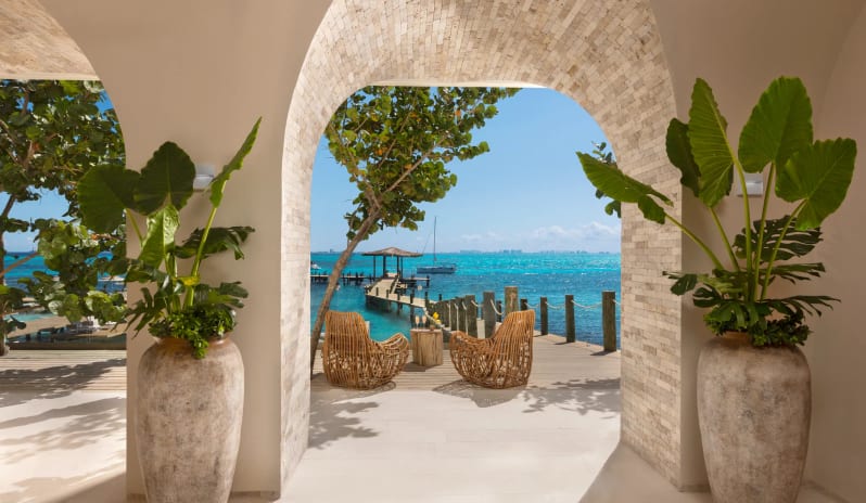 Yacht Welcome Lounge waterfront welcome lounge framed by an elegant stone archway overlooking a tropical ocean pier at Impression Isla Mujeres by Secrets by Kenwood Travel