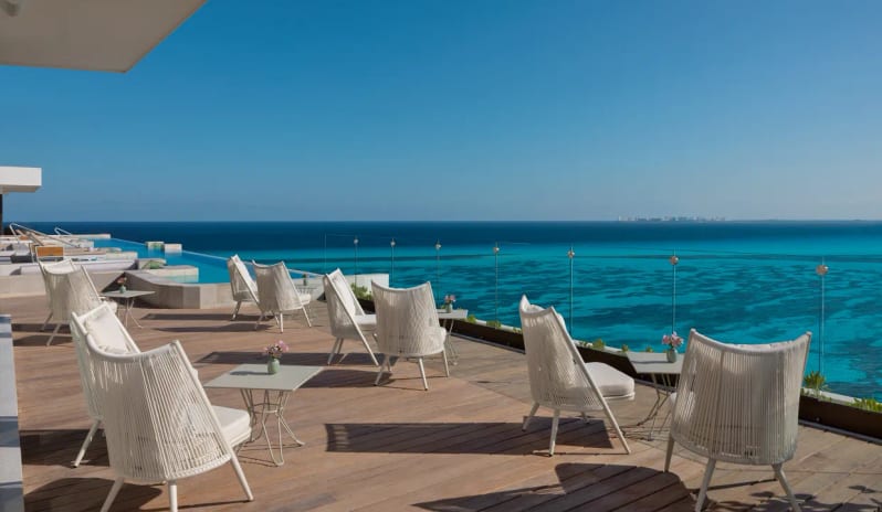 Unik the Kitchen routdoor dining terrace with stylish white chairs and sweeping ocean views at Impression Isla Mujeres by Secrets by Kenwood Travel