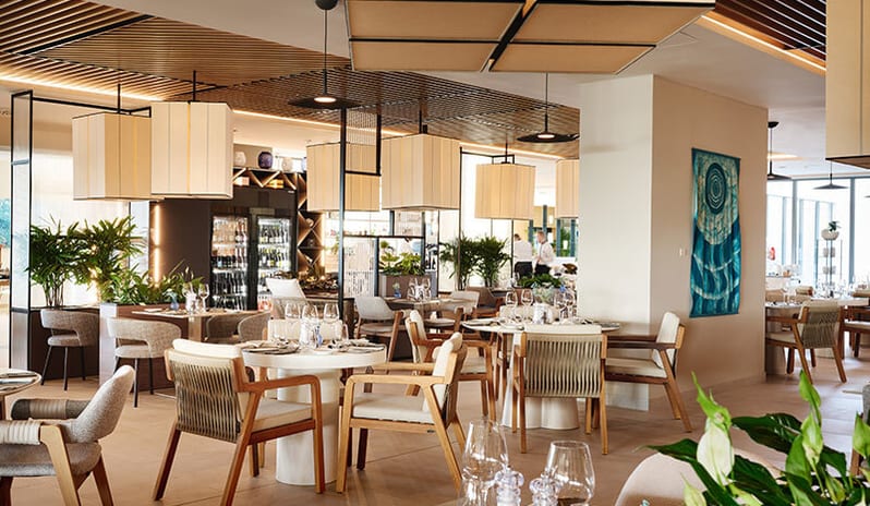 More Restaurant with square fabric lamps, slatted wooden ceilings, lush indoor plants, and fine dining table setups at Pical Resort, Valamar Collection by Kenwood Travel