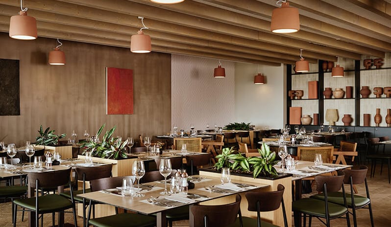 Quattro Terre warm terracotta pendant lighting, wooden ceiling beams, and set tables with potted green plants at Pical Resort, Valamar Collection by Kenwood Travel