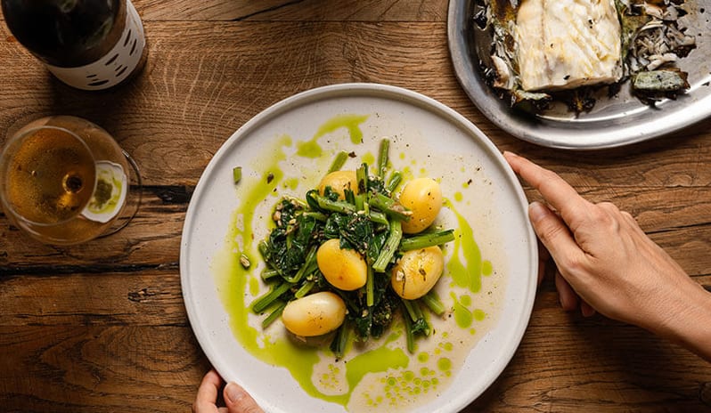 Fogo by Bekal plated dish of potatoes, leafy greens, and roasted fish on a wooden table at Pical Resort, Valamar Collection by Kenwood Travel