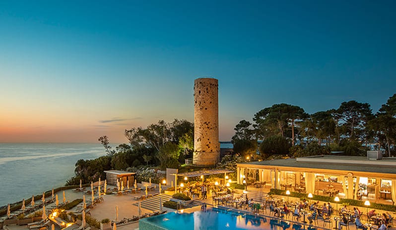 Miramare Restaurant by Fratelli Cerea Sunset view over the sea with guests dining by the illuminated infinity pool at Pical Resort, Valamar Collection by Kenwood Travel