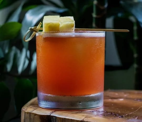Waitiki Tropical tiki cocktail garnished with pineapple cubes on a wooden block at Moon Palace The Grand Punta Cana by Kenwood Travel
