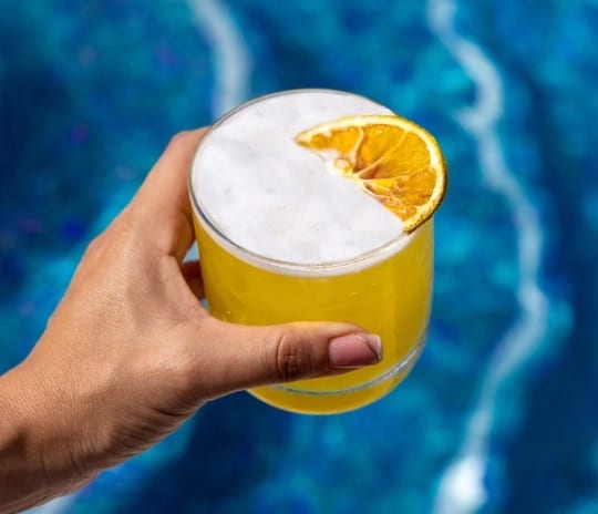 Unique Day Club Fresh citrus cocktail garnish held above a blue resort swimming pool at Moon Palace The Grand Punta Cana by Kenwood Travel