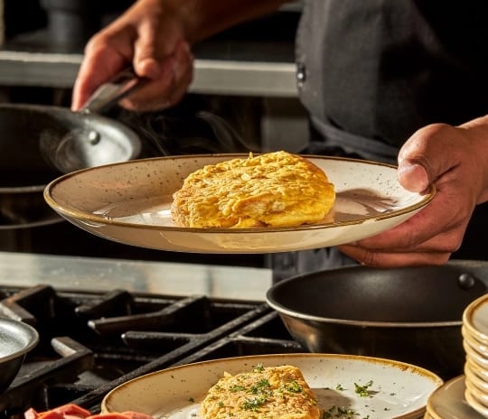 Casa Macao Chef plating a fluffy golden egg omelet at an interactive live cooking station at Moon Palace The Grand Punta Cana by Kenwood Travel