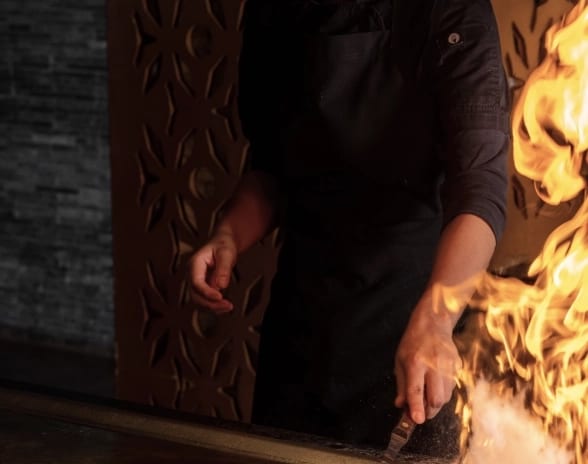 Teppan by Momo Teppanyaki chef performing a live flame cooking demonstration on a iron flat grill at Moon Palace The Grand Punta Cana by Kenwood Travel