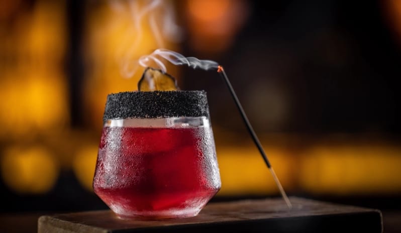 Madremía Smoky red craft cocktail with a black salt rim and burning incense stick at Moon Palace The Grand Punta Cana by Kenwood Travel