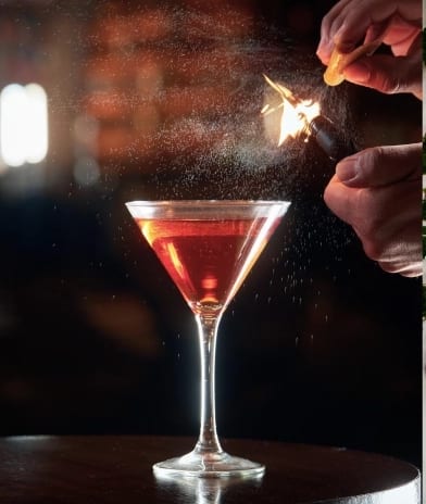 Speakeasy Bar Bartender expressing and flaming an orange peel over a craft martini cocktail at Moon Palace The Grand Punta Cana by Kenwood Travel