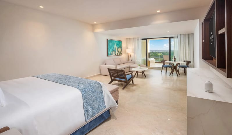 Grand Family Suite Golf View king bed, living area with sofa, small dining set, and open terrace overlooking the golf course at Moon Palace The Grand Punta Cana by Kenwood Travel