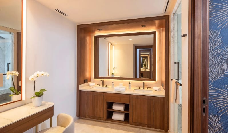 Grand Family Suite Ocean View bathroom with a double wooden vanity, large LED backlit mirror, plush white towels, and a separate makeup table with an upholstered chair at Moon Palace The Grand Punta Cana by Kenwood Travel