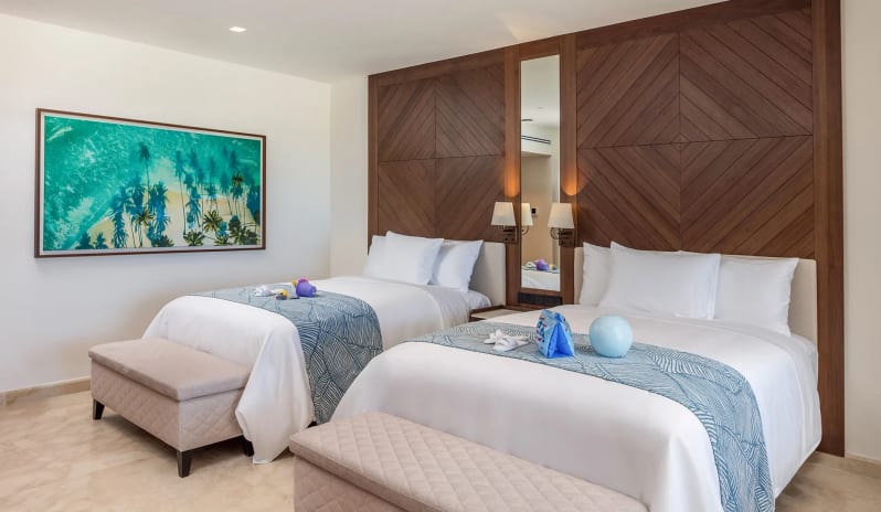 Grand Family Suite Ocean View two double beds with blue pattern runners, padded footrest benches, and tropical artwork at Moon Palace The Grand Punta Cana by Kenwood Travel