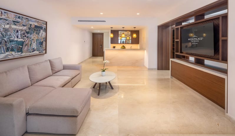 Grand Governor Suite Ocean View large sectional sofa, coffee table, wall-mounted TV console, and illuminated wet bar in the background at Moon Palace The Grand Punta Cana by Kenwood Travel