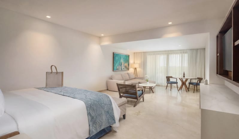 Grand Swim-up Suite king bed, living room seating area, dining space, and large patio doors at Moon Palace The Grand Punta Cana by Kenwood Travel