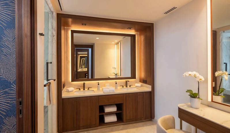 Grand Swim-up Suite bathroom featuring a wooden double vanity with backlit mirrors and a vanity makeup desk with a chair at Moon Palace The Grand Punta Cana by Kenwood Travel