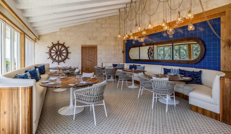 Regatta dining area with white booths, round tables, nautical decor, and a blue tiled accent wall at Salterra, A Luxury Collection Resort & Spa, South Caicos by Kenwood Travel