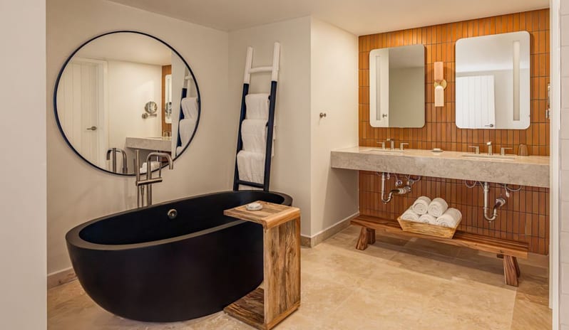 One Bedroom Ocean View King Suite Lanai Patio bathroom with a black freestanding tub, round wall mirror, and double sink vanity at Salterra, A Luxury Collection Resort & Spa, South Caicosby Kenwood Travel