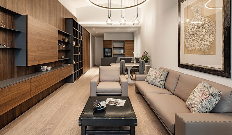 Lake View Loggia Suite living room with built-in dark wood shelving, plush beige sofa, ring chandelier, and open dining space in the background at ARIA Retreat & SPA by Kenwood Travel