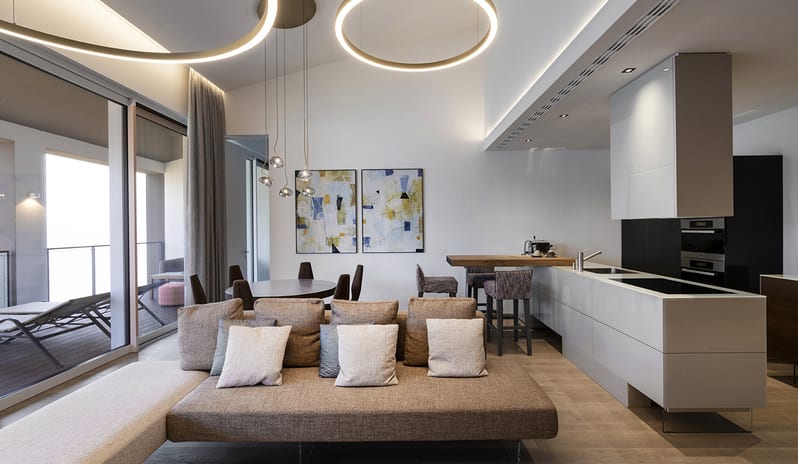 Lago Penthouse Suite living area featuring contemporary minimalist furniture, large ring ceiling lights, and an adjacent balcony terrace at ARIA Retreat & SPA by Kenwood Travel