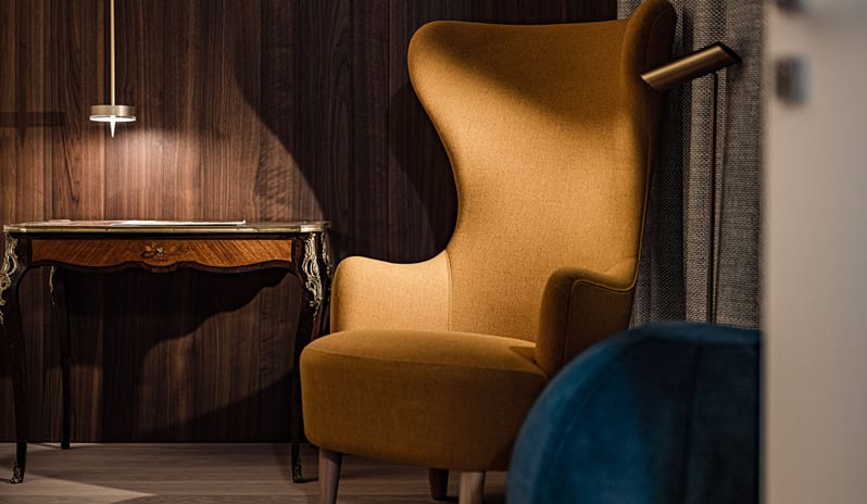 Lake View Grand Loggia Suite Luxury hotel suite seating corner with a modern mustard yellow high-back armchair, warm brass pendant lamp, and antique wooden side desk at ARIA Retreat & SPA by Kenwood Travel