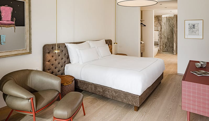 Lake View Loggia Suite bedroom with plush white bedding, tufted brown headboard, stylish leather lounge chair, and adjacent marble bathroom at ARIA Retreat & SPA by Kenwood Travel