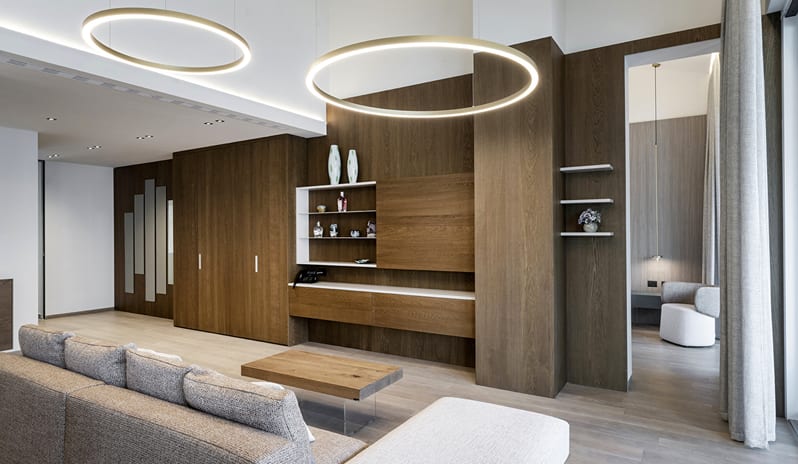 Lago Penthouse Suite Large circular halo pendant lights suspended above a minimalist living room featuring warm wood finishes and neutral tones at ARIA Retreat & SPA by Kenwood Travel