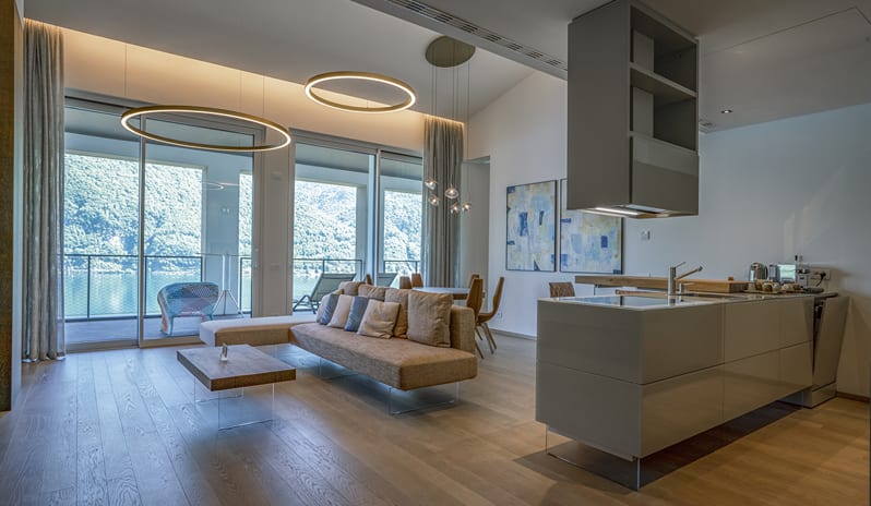 Lago Penthouse Suite living area featuring contemporary minimalist furniture, large ring ceiling lights, and an adjacent balcony terrace at ARIA Retreat & SPA by Kenwood Travel