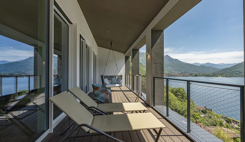 Lago Penthouse Suite Covered balcony deck with beige sun loungers, mesh safety railings, and a suspended swing chair overlooking a lake at ARIA Retreat & SPA by Kenwood Travel