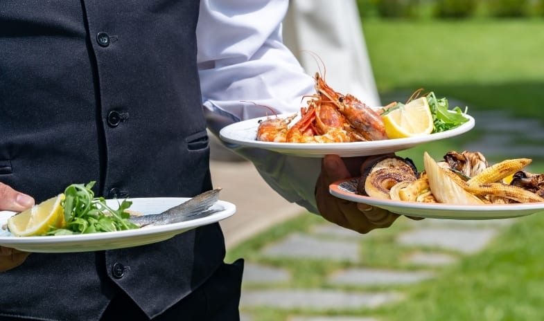 46° Parallelo Close-up of a waiter serving gourmet grilled seafood plates outdoors at a luxury venue at ARIA Retreat & SPA by Kenwood Travel