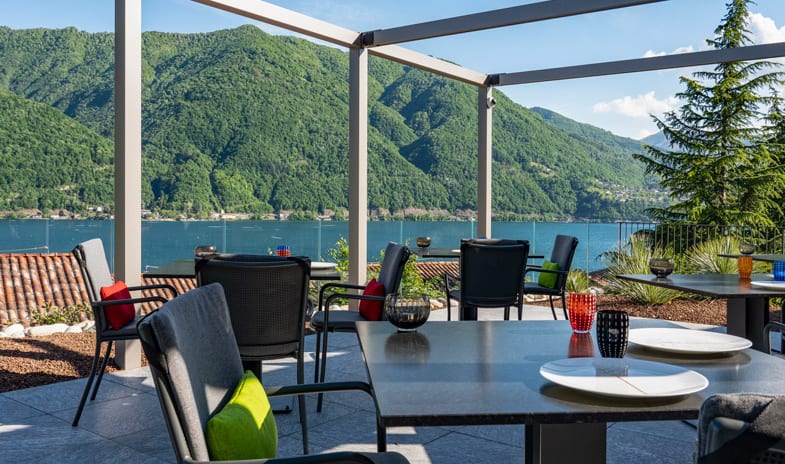La Musa Restaurant & Rooftop Terrace Grey metal pergola covering an outdoor dining patio with contemporary furniture facing a mountain lake at ARIA Retreat & SPA by Kenwood Travel