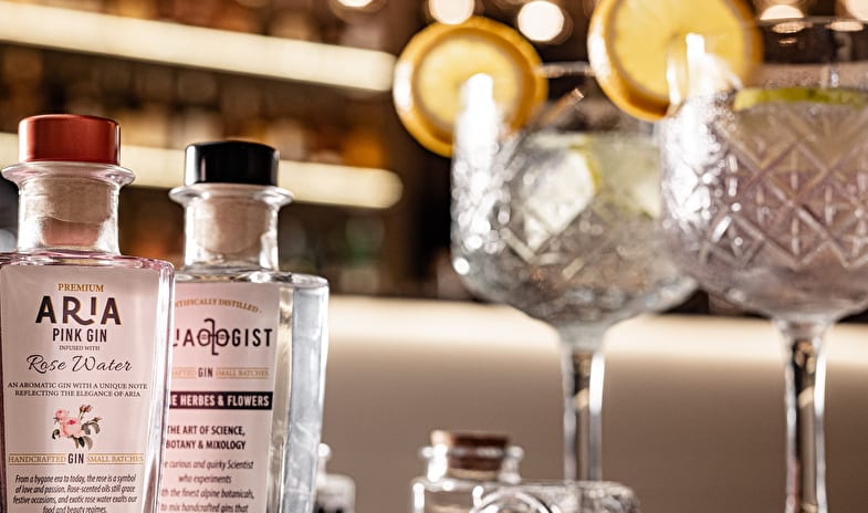 Dolce Vita Lounge & Terrace Handcrafted gin bottles and crystal gin and tonic glasses served on a bar counter with warm bokeh background lighting at ARIA Retreat & SPA by Kenwood Travel
