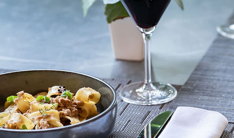 La Joie de Vivre Restaurant Gourmet Italian pasta dish paired with red wine, set on a modern dining table with place mat and napkin at ARIA Retreat & SPA by Kenwood Travel