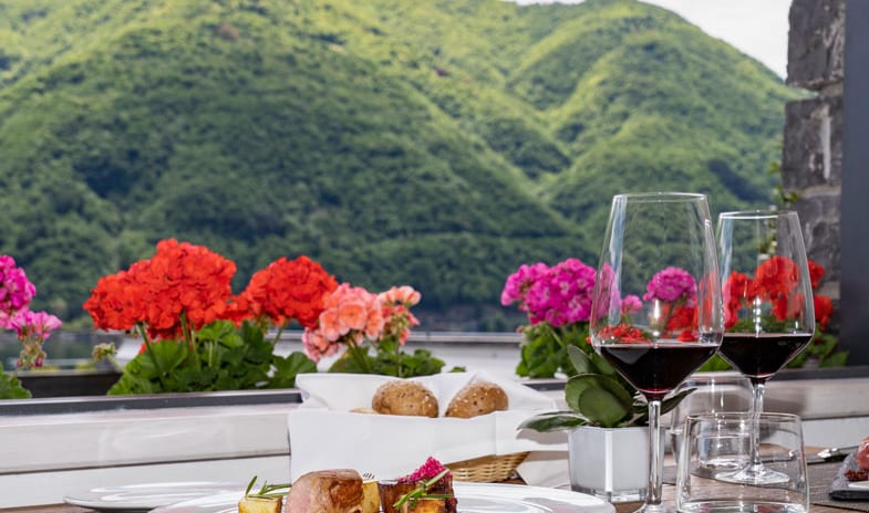 La Masseria Restaurant Gourmet dish and red wine on an outdoor restaurant table overlooking lush green mountains at ARIA Retreat & SPA by Kenwood Travel