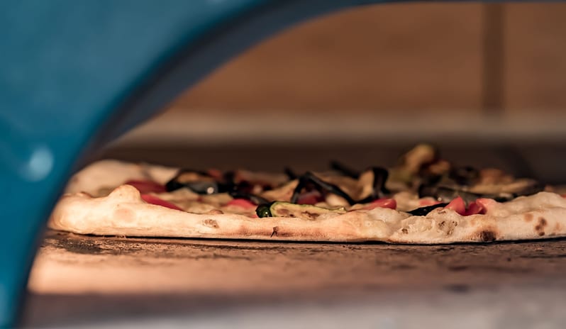 Il Basilico - La Pizzeria A close-up view of an artisan vegetable pizza with a crisp, blistered crust baking inside a stone-deck pizza oven at ARIA Retreat & SPA by Kenwood Travel