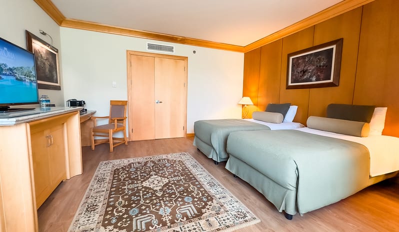Family Suite two two single beds with sage green linens, wood-paneled walls, an patterned area rug, and a TV console at Gloria Verde by Kenwood Travel