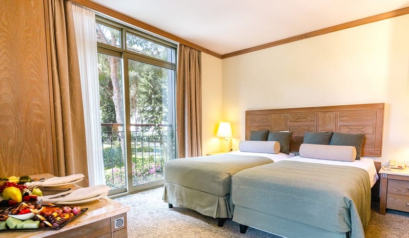 Family Suite two single beds with sage green bedding, a large wooden headboard, and glass sliding doors opening to a balcony at Gloria Verde by Kenwood Travel