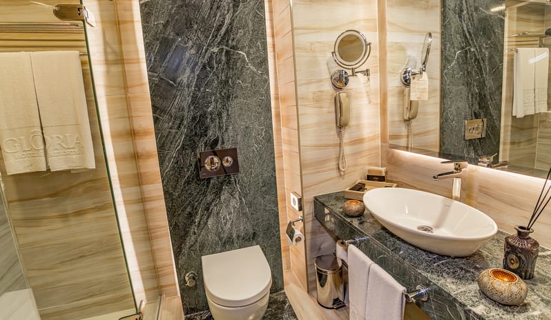 Standard Room white vessel sink on a dark marble countertop, a large mirror, a toilet, and dark marble accent walls at Gloria Verde by Kenwood Travel