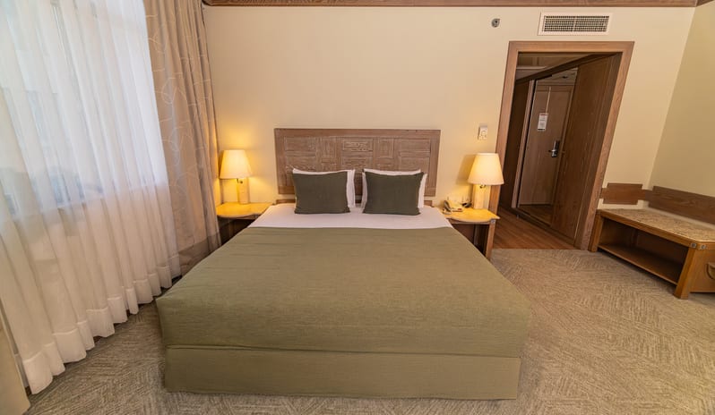 Standard Room double bed with green bedding, wooden headboard, and bedside lamps at Gloria Verde by Kenwood Travel