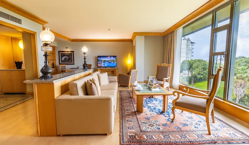 King Suite living area showcasing hardwood floors, a dividing counter with decorative lamps, a TV console setup, and expansive floor-to-ceiling windows at Gloria Verde by Kenwood Travel