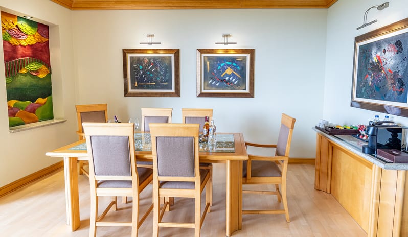 King Suitelight wood dining table with six upholstered chairs, abstract wall art, and a side console table with a coffee machine at Gloria Verde by Kenwood Travel