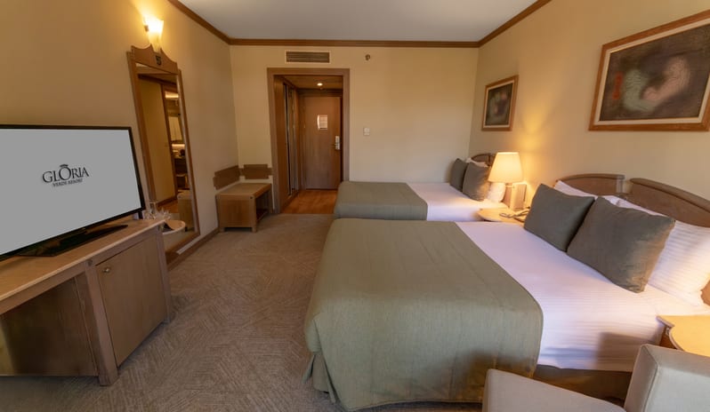 Standard Room two double beds with green runners, a flat-screen TV, and warm lighting at Gloria Verde by Kenwood Travel