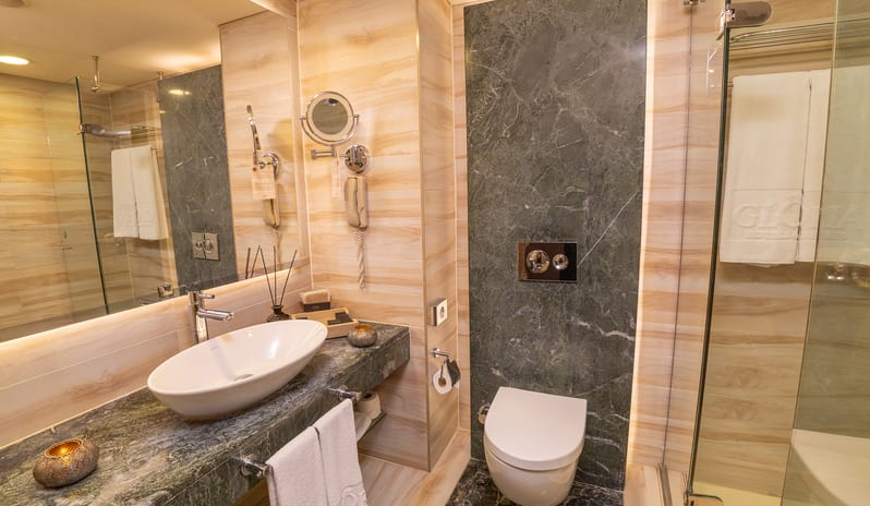 Standard Room marble vanity with a vessel sink, a large mirror, a wall-mounted toilet, and a glass shower enclosure at Gloria Verde by Kenwood Travel