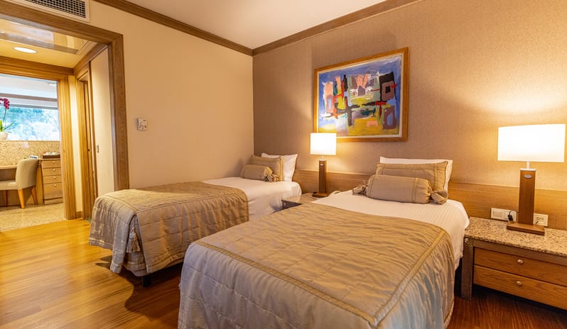 Select Villa two single beds, hardwood floors, abstract wall art, and an adjacent vanity room at Gloria Verde by Kenwood Travel