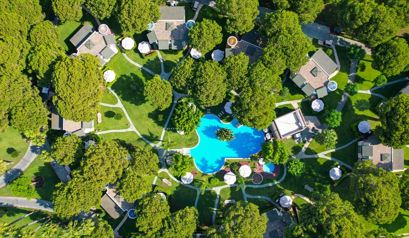Select Villa surrounded by lush green trees, winding pathways, and a large, uniquely shaped swimming pool at Gloria Verde by Kenwood Travel