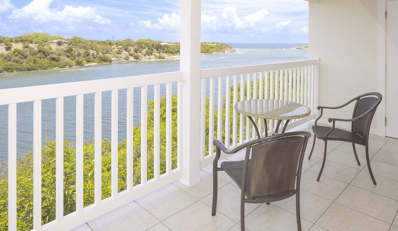 Waterfront Suite balcony with table and seating overlooking a scenic water and bay view at The Verandah Antigua by Kenwood Travel