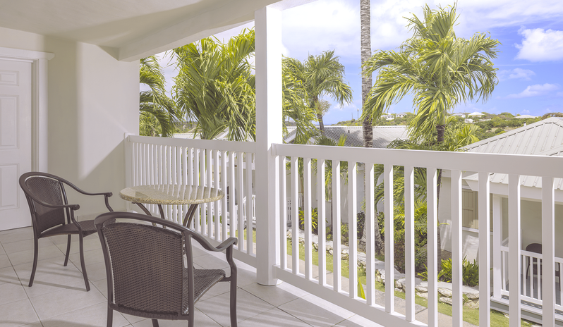 Hillside Suite Garden/Resort Views balcony with table and chairs overlooking tropical palm trees at The Verandah Antigua by Kenwood Travel