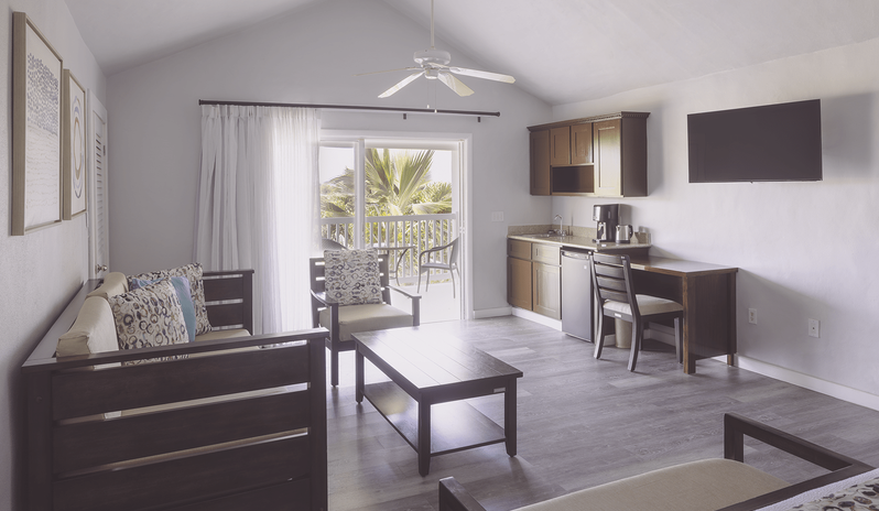 Water View Suite living room with kitchenette, sofa, and sliding door to a balcony at The Verandah Antigua by Kenwood Travel