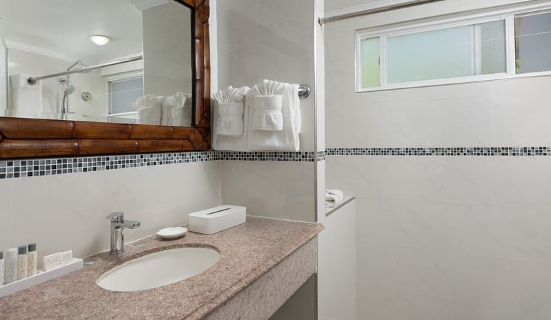Garden View bathroom vanity with granite countertop, large wooden mirror, and white tiled wall at The Club Barbados Resort & Spa by Kenwood Travel