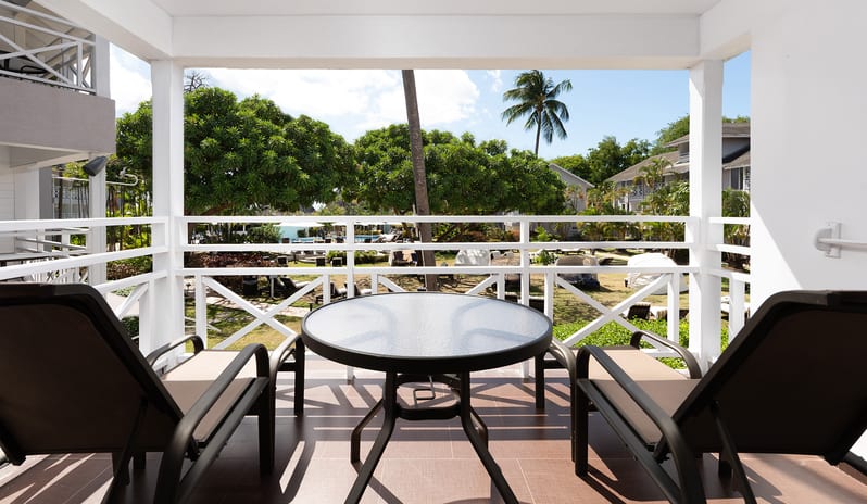 One Bedroom Pool Garden View Suite balcony with loungers and a table overlooking tropical garden grounds at The Club Barbados Resort & Spa by Kenwood Travel