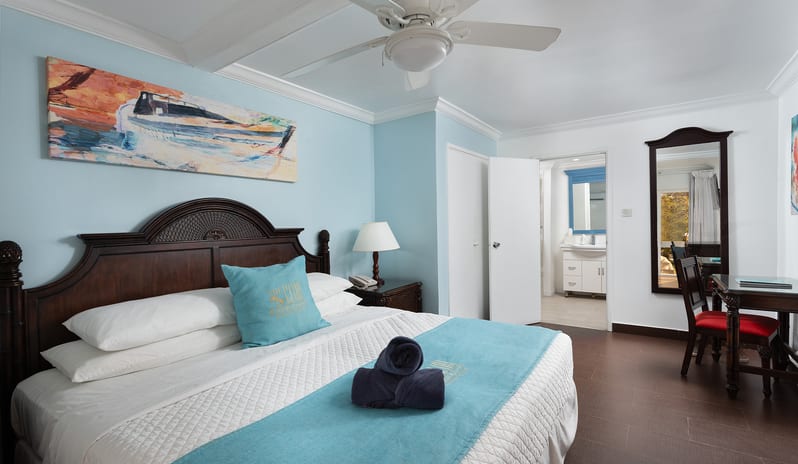 One Bedroom Pool Garden View Suite bedroom with dark wood nightstands and large window with garden view at The Club Barbados Resort & Spa by Kenwood Travel